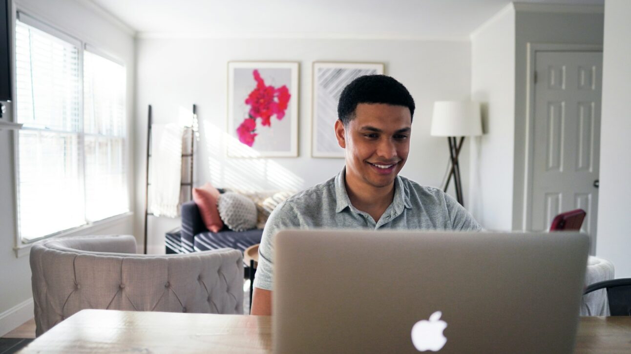 man in gray hoodie sitting on chair in front of silver macbook